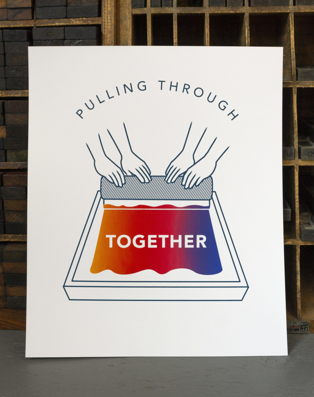 White paper print with screenprinted illustration of two pairs of hands pulling a squeegee on a screen with the word 'Pulling Through Together'. The words pulling through is laid out in an arch above the hands, and the word together is in the screen. The ink in the screen is a gradient of orange, red, pink and blue.