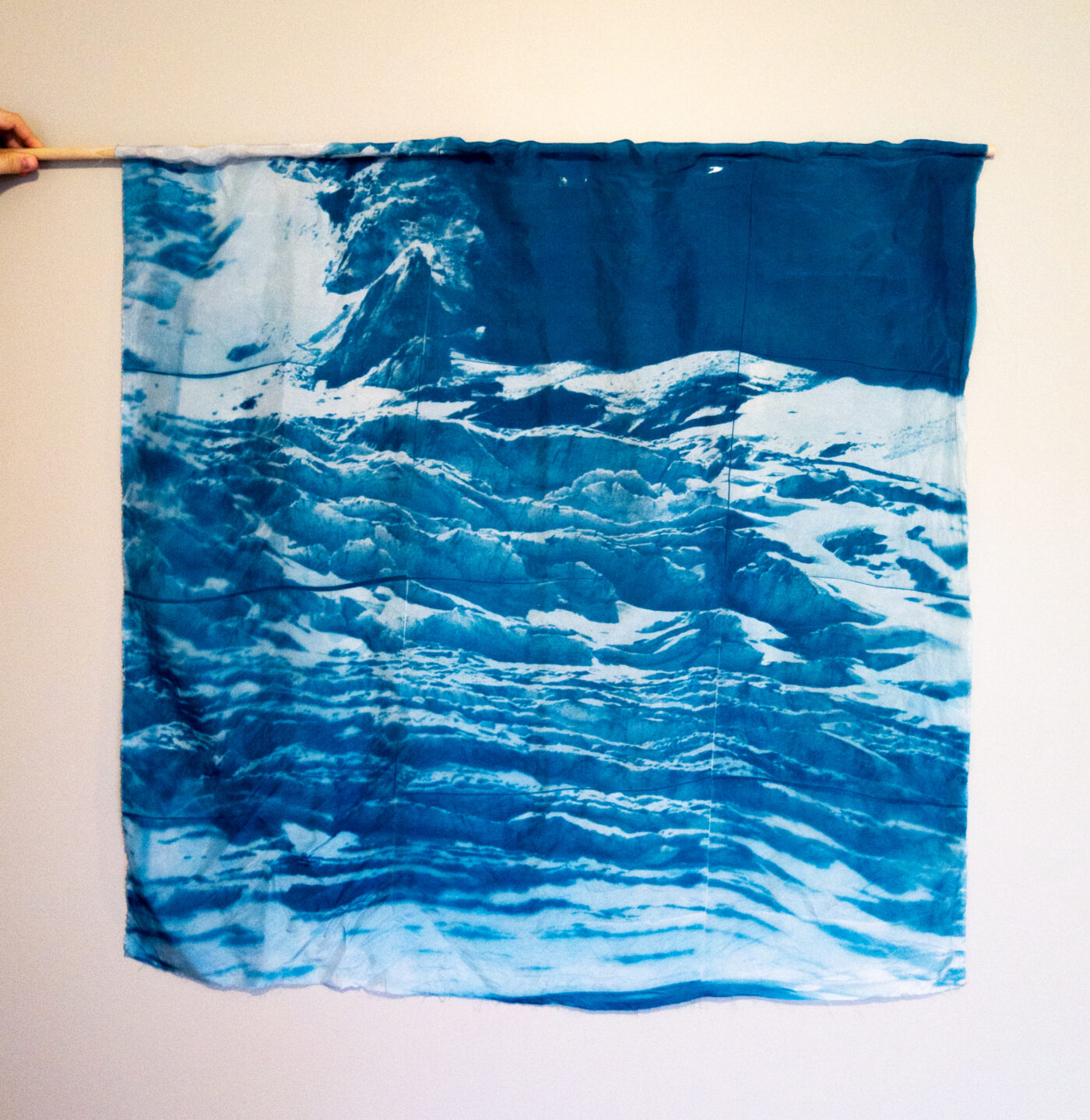 a cyanotype print showing the athabasca glacier, hung from a small rod to look like a square flag