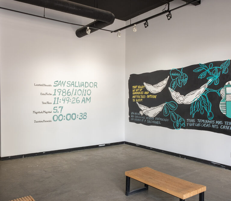 Work by Michelle Campos in a gallery, featuring two white walls with murals painted. The murals are laid out like comic panels, detailing Michelle's experience in the aftermath of an earthquake in Salvador.