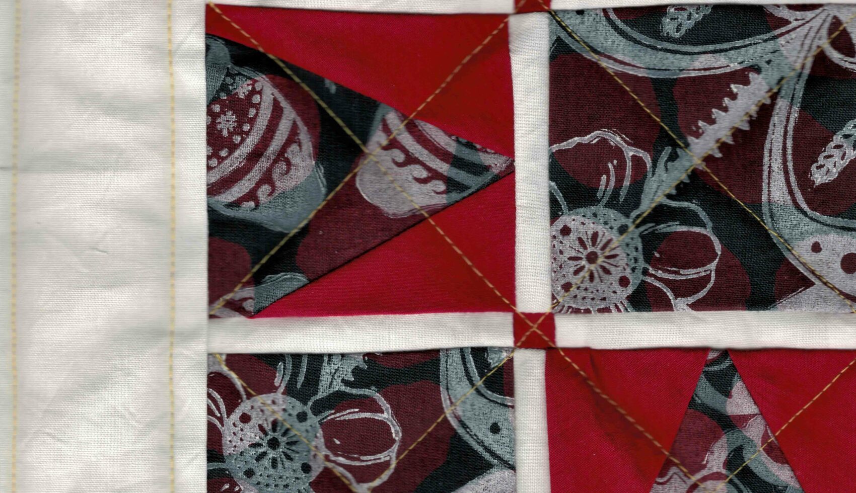Cropped view of a quilt with squares of printed fabric and red triangles forming a square star. The squares feature a deep red bAckground and dark blue floral patterns reminiscent of Ukrainian traditional art.