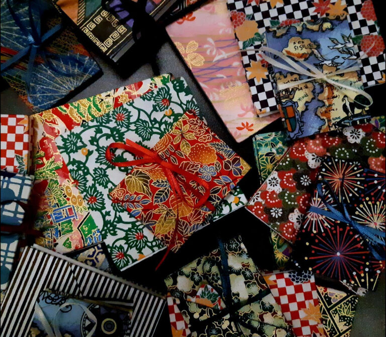 Many colourful handmade books with vibrant patterns are strewn about on a table